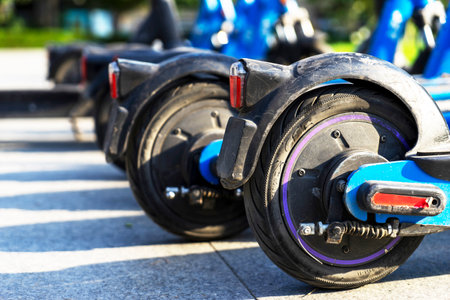 Blue electric scooters parked in the parking lot are ready for use - this is a very familiar vehicle that allows you to move around without polluting the environment. Environmentally friendly transport. Wheels in close-up.の写真素材