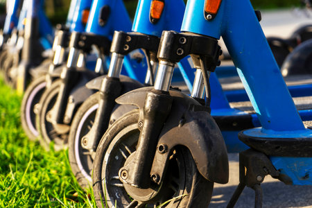 Rented blue electric scooters parked in the parking lot are ready for use - this is a very familiar vehicle that allows you to move around without polluting the environment. Environmentally friendly transport. Wheels in close-up.の写真素材