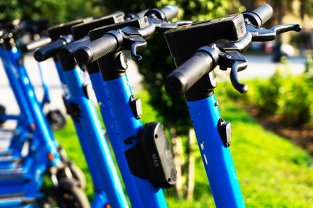 Rented blue electric scooters parked in the parking lot are ready for use - this is a very familiar vehicle that allows you to move around without polluting the environment. Environmentally friendly transport. Close-up of the steering wheelの写真素材