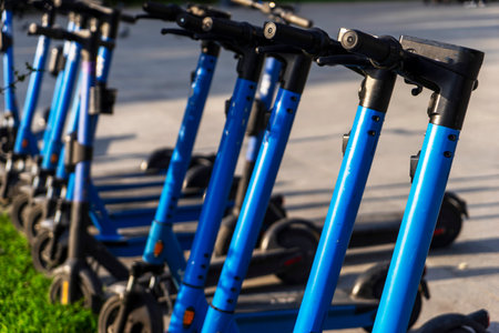 Rented blue electric scooters parked in the parking lot are ready for use - this is a very familiar vehicle that allows you to move around without polluting the environment. Environmentally friendly transport. Close-up of the steering wheelの写真素材
