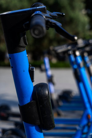 Rented blue electric scooters parked in the parking lot are ready for use - this is a very familiar vehicle that allows you to move around without polluting the environment. Environmentally friendly transport. Close-up of the steering wheelの写真素材