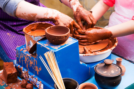 Hands of male potter, ceramist making of an earthenware pot. Potter teaches the student to make a pitcher on a pottery wheel.の写真素材