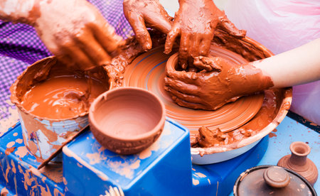 Hands of male potter, ceramist making of an earthenware pot. Potter teaches the student to make a pitcher on a pottery wheel.の写真素材