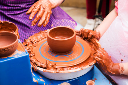Hands of male potter, ceramist making of an earthenware pot. Potter teaches the student to make a pitcher on a pottery wheel.の写真素材