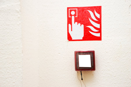 Fire alarm button encased in glass over a sign showing a finger pushing the button near flamesの写真素材