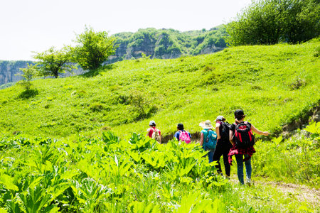 A group of people with backpacks walking along the road. There are mountains on the horizon. The sky is blue and cloudy.の写真素材