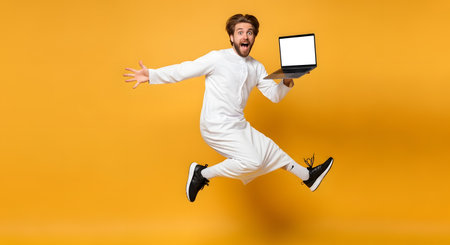 A dynamic image capturing a young man in a white thobe joyfully jumping with a laptop, embodying excitement and technological engagement.の素材