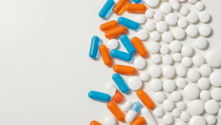 A varied assortment of white round tablets and colorful orange and blue capsules are arranged on a white surface.の素材