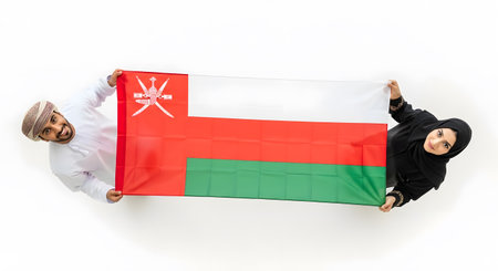 Two people hold up the flag of Oman, showcasing national pride and cultural heritage against a plain background.の素材