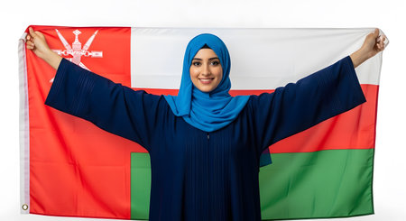A young Muslim woman wearing a hijab smiles while holding the Omani flag, showing national pride and cultural representation.の素材
