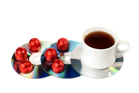 A cup of tea with sweets on CDs. Isolated on white background.
