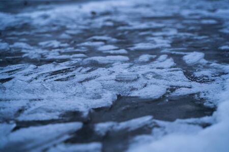 Winter abstract texture close up of frozen water of lake shore. White blue black scenery background.