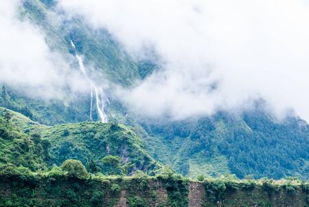 Picture of the waterfall in Himalayas mountains. Green hills with forest behind the clouds. Hiking,...
