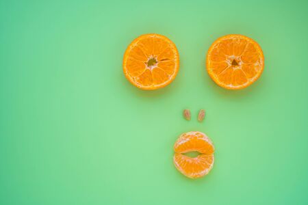 Tangerine slices as a funny muzzle on green mint background. Fresh vegan food.