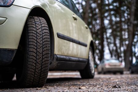 Close up front view of a family car on parking with another cars on background. Dirty front wheel...