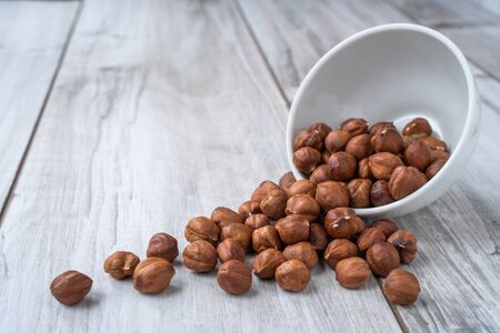 Scattered hazlenuts with white bowl on lignt wood table with copy space. Stock photoの写真素材
