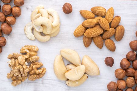 Different nuts piles on wooden table. Nuts background. Hazlenuts, walnuts, almond, brazilian and...