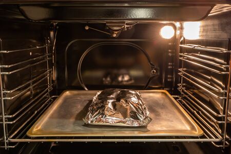 Food covered with foil on the pan inside gas oven ready for cooking. Stock photoの写真素材