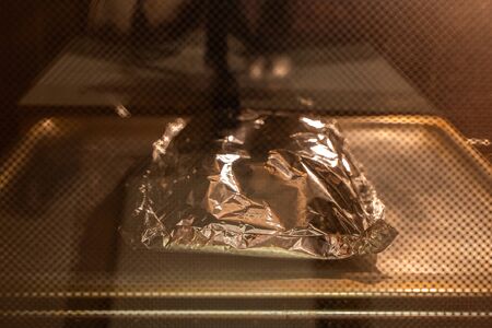 Food covered with foil on the pan inside gas oven ready for cooking. Stock photoの写真素材