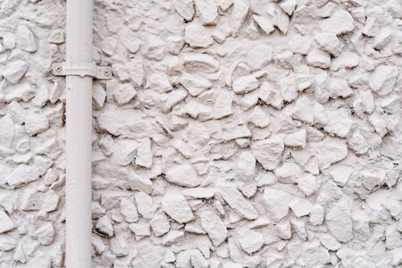 Texture of a wall covered with rubble stone painted with light stain with water pipe, abstract...