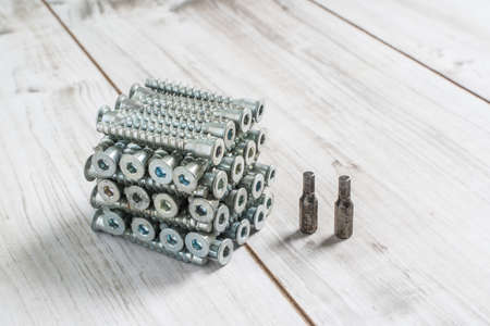 Group of Screw bolts for furniture assembling organized in stack on wooden background. Stock photo.