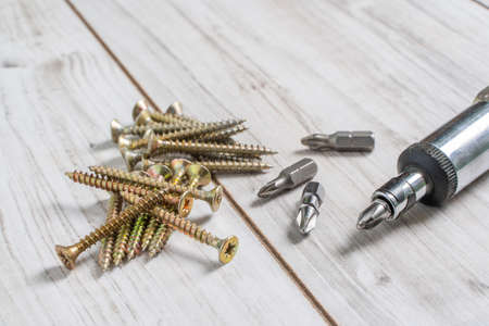 Metal Screws organized in stack with screwdriver and screwdriver heads (bits) on wooden background....