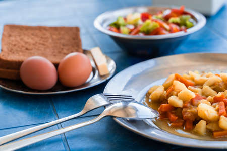 Simple Rustic Food Breakfast Set. Stewed Potatoes with Carrots, Vegetable Salad, Boiled Eggs, Bread and Butter. Stock Photo.の写真素材