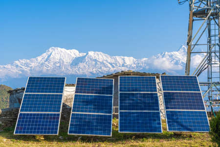 Solar panels near telecommunication tower in the mountain region. Snow covered mountain peaks on background. Green and environmentally friendly sources of energy. Stock photoのeditorial素材