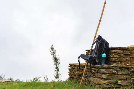 Backpack with water bottle and bamboo stick on stone fence near chasm. Mountains are hidden by clouds. Hiking and trekking concept.の写真素材