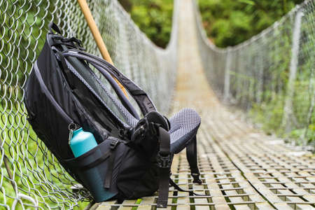 Backpack with water bottle and bamboo stick on pedestrian suspension bridge. Mountain hiking,...