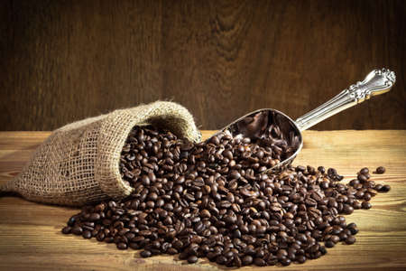 Coffee beans on burlap sack with metal scoop on old plankの写真素材