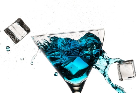 Ice cubes breaking martini glass filled with blue liqueur on white backgroundの写真素材