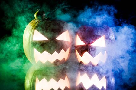 Two pumpkins for Halloween on blue and green smokeの写真素材