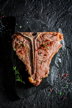 Yummy tbone steak on black rock with herbs and pepperの写真素材