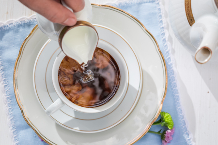 Pouring milk into coffee on a white tableの写真素材