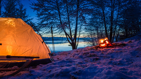 Sunset at the lake with tent and bonfire in winterの写真素材