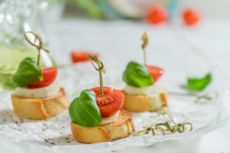 Tasty crostini made with mozzarella and tomato on white paperの写真素材