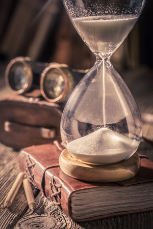 Closeup of hourglass and journal with compass and binocular