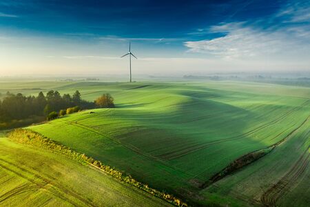 Wind turbine on foggy green field at sunriseの写真素材
