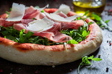 Fresh pizza Parma with prosciutto, arugula and parmesan on wooden tableの写真素材