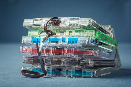 Pile of vintage cassette tapes with an extracted tape on blue sofa