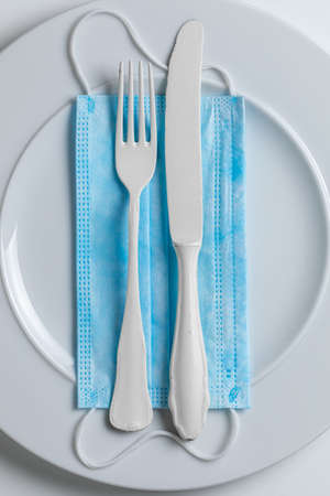 Protective mask and empty plate as restrictions in coronavirus pandemic on white background. Covid-19 conceptの写真素材