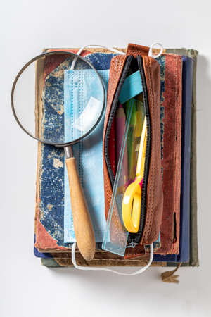 Protective mask, pencil case and magnifying glass on white background. Pandemic limitation