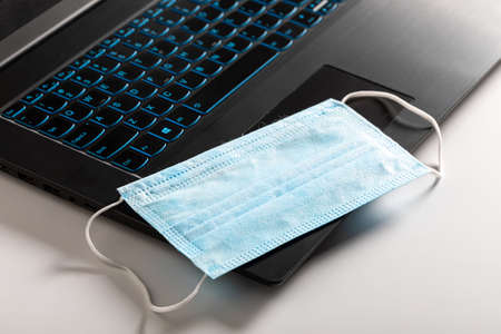 Home work during Covid 19 pandemic. Computer and blue mask on white backgroundの写真素材