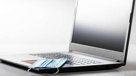 Disposable face mask and laptop on white background. Remote work during Covid 19 pandemic.
