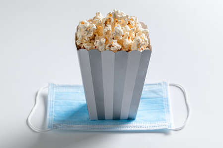 Concept of COVID-19 and protective in cinema. Popcorn and disposable mask on white backgroundの写真素材