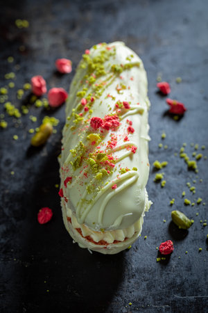 Sweet eclairs with dry pistachios and strawberries on baking tray