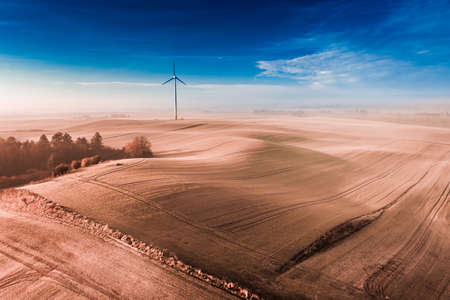 Wind turbine on foggy brown field at sunrise, aerial view of Poland