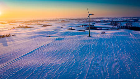 Amazing snowy field and wind turbine at sunrise in winter, aerial view