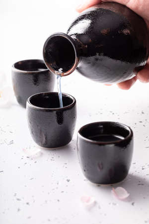 Unfiltered sake with blooming cherry. Japanese habit of drinking alcohol. Black ceramics on a white stone.の写真素材